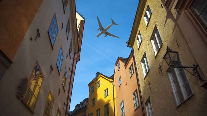 Ett flygplan syns på himlen mellan stora huskroppar.