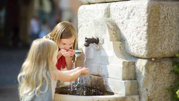 Två små flickor dricker vatten i en fontän av sten.
