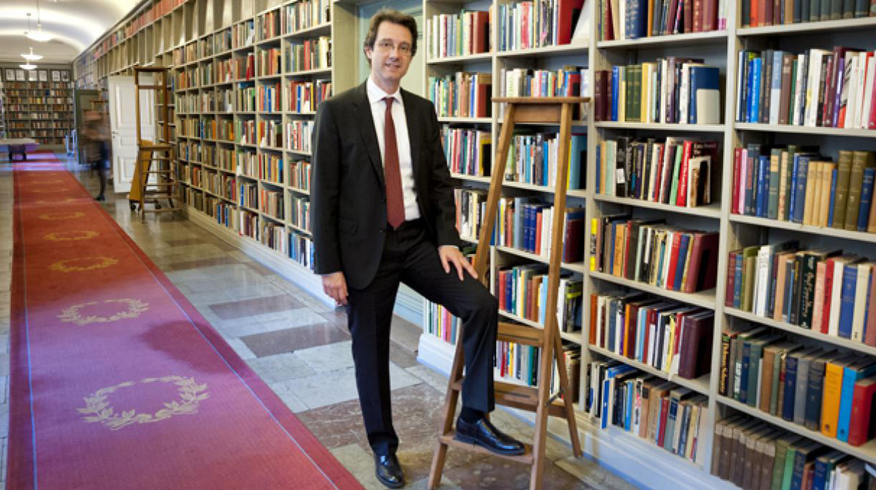 Tomas Riad står vid en bokhylla med ena foten på en stege.