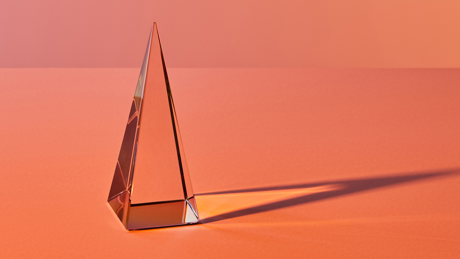 Genomskinlig spetsig glaspyramid. Även skuggan syns mot botten av tre olika orange nyanser.