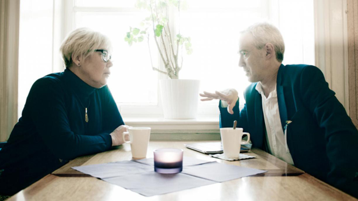 Berit Högman och Gustaf Arrhenius sitter vid ett cafébord och pratar med varandra.