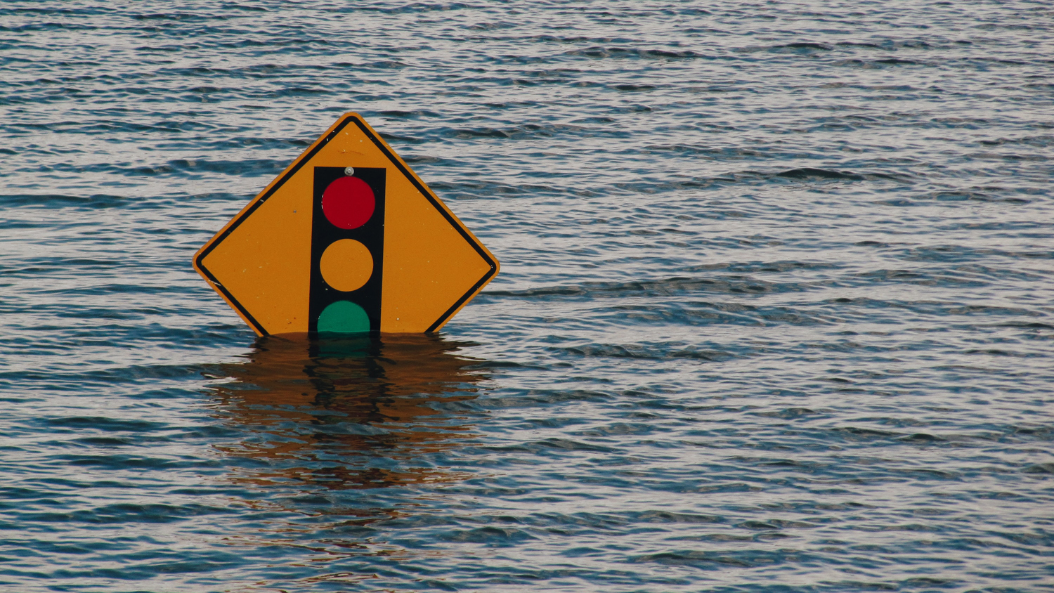 Den översta delen av en gul vägskylt med trafikljussymbol sticker upp ovanför vattenytan.