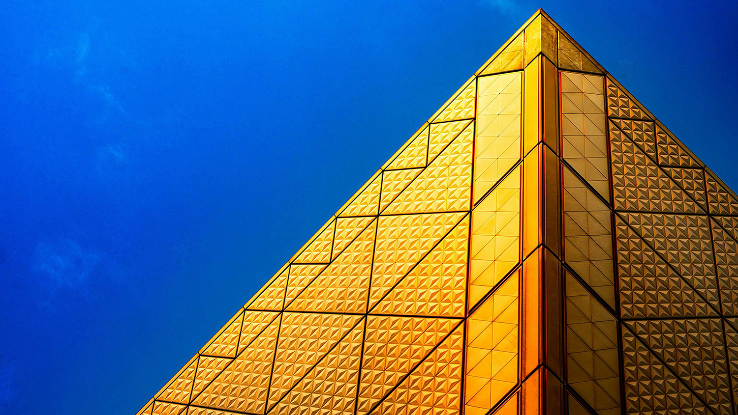 Gyllene pyramidformad byggnad mot blå himmel.