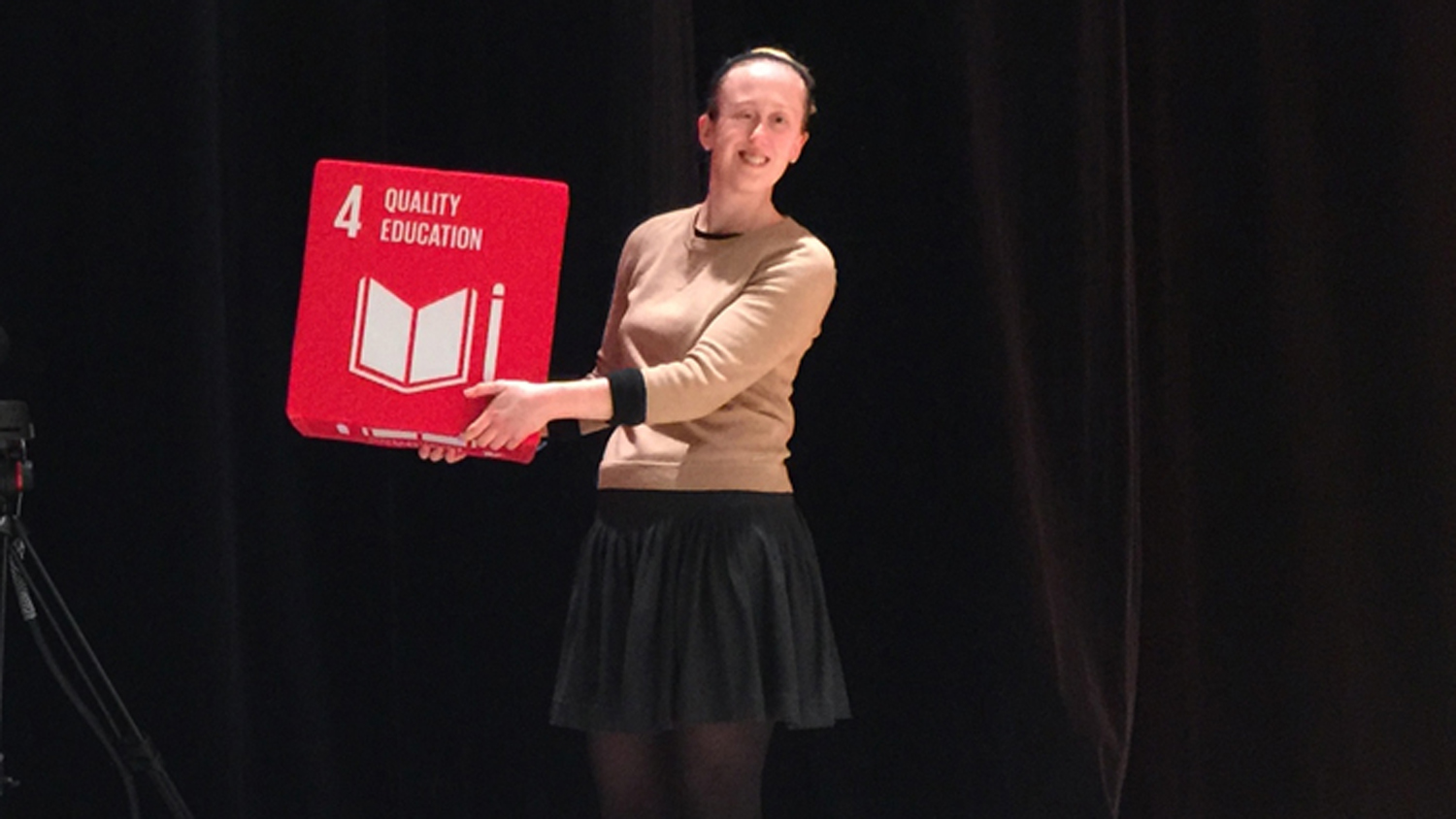 Anna Ilar.står på en scen och visar upp en stor kub som det står Quality Education på.