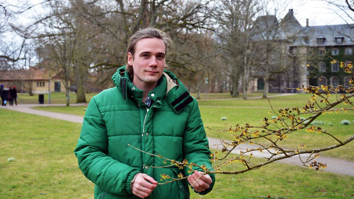 Jonatan Leo står i grönområde och håller trädgren i handen.