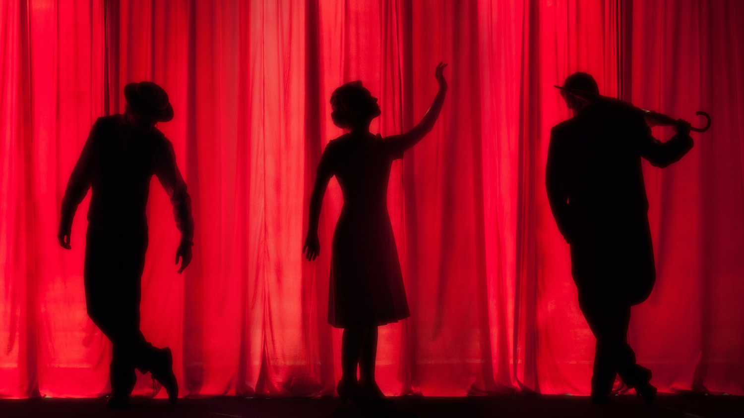 Tre svarta siluetter på scen framför en röd ridå.
