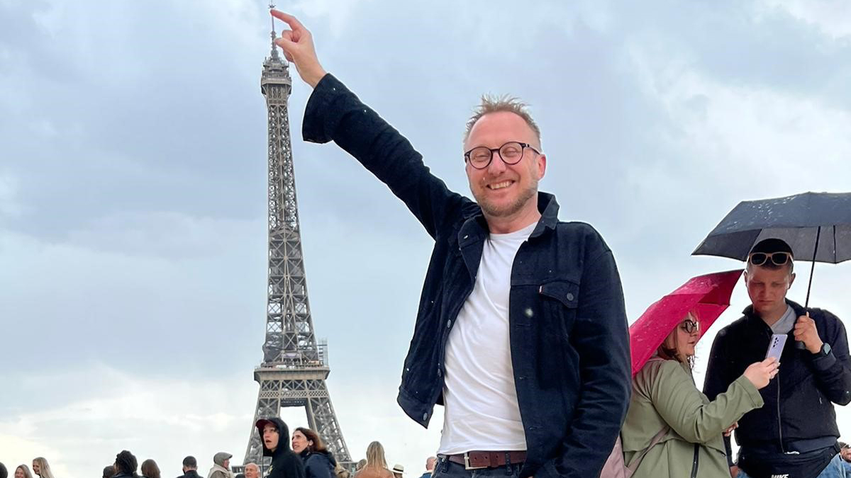 Bengt Johansson står framför Eiffeltornet och pekar mot tornets topp.