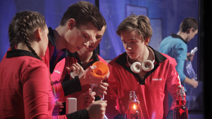 Fyra ungdomar i röd klädsel som labbar i kemi.