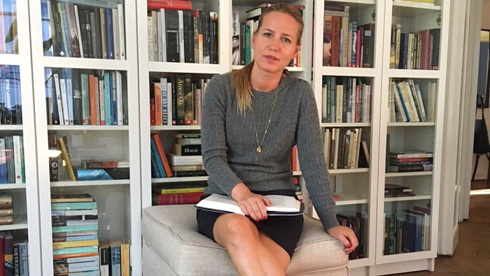 Anna Victoria Hallberg sitter framför en bokhylla med en bok i sitt knä.
