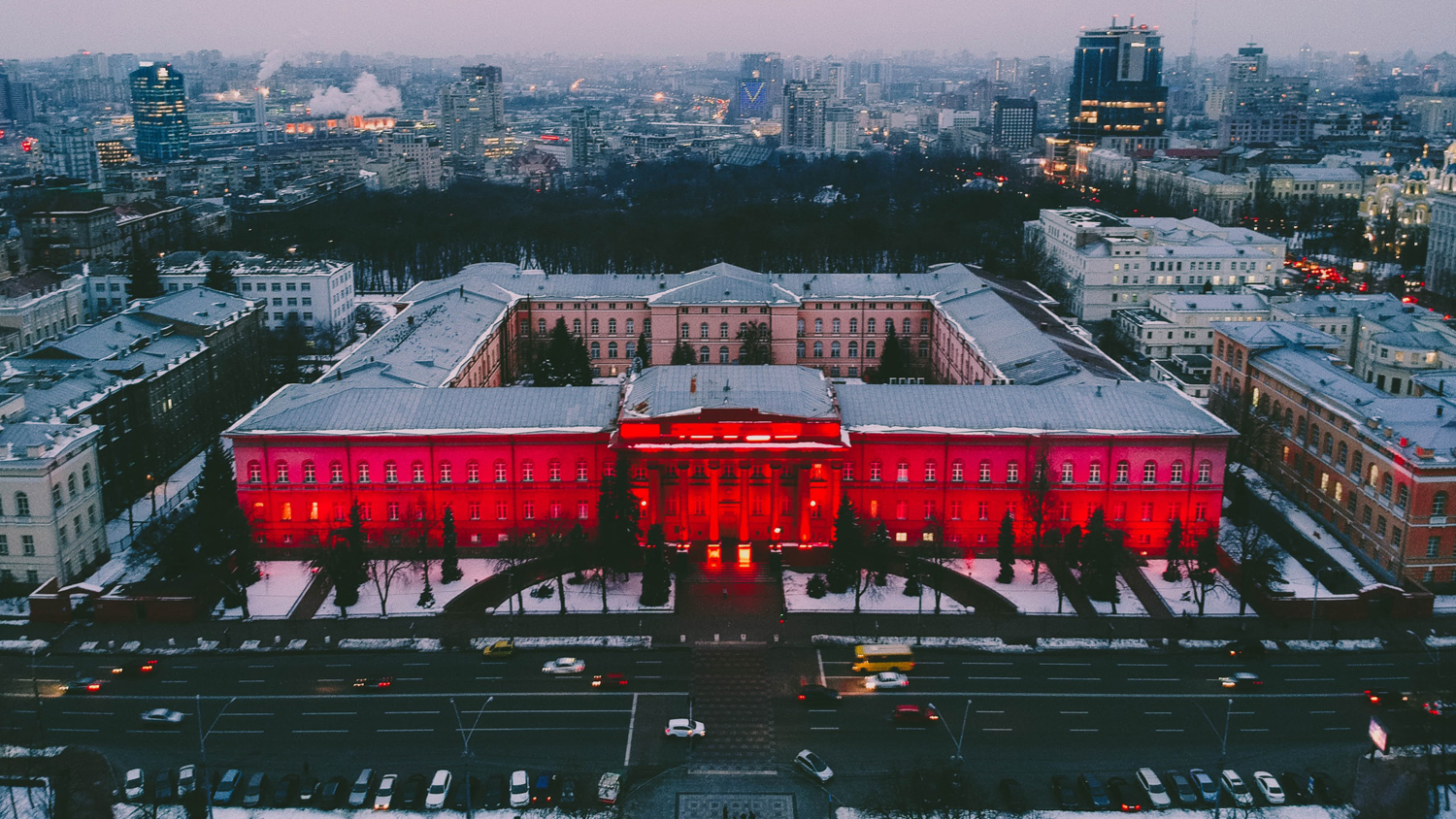 Stadsbild med universitetet i Kyiv i fokus. Byggnaden är upplyst i rött. 