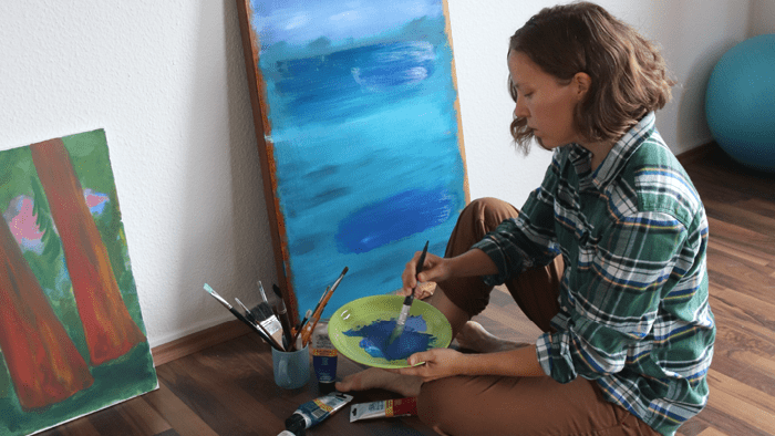 Marina Rantanen Modeer sitter framför sin målning med en pensel i handen.