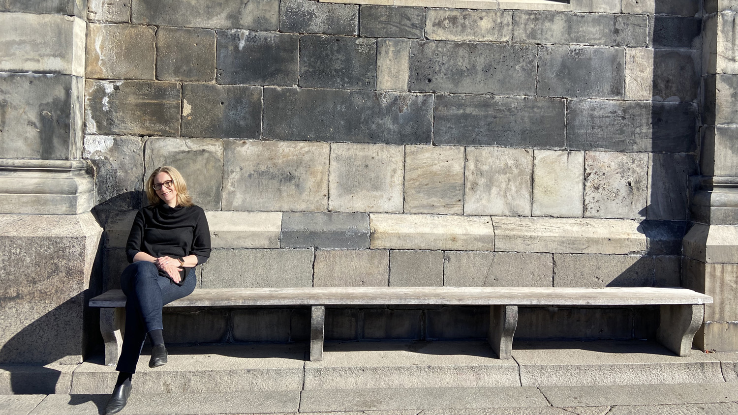 Marie Cronqvist sitter på en stenbänk i solen.