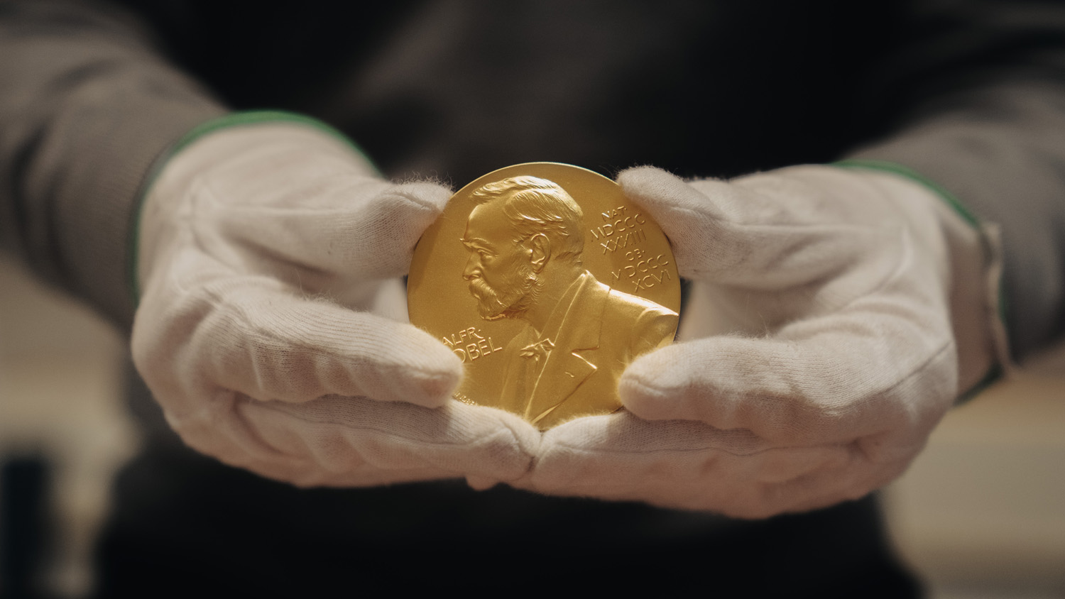 Handskbeklädda håller i en Nobelprismedalj.