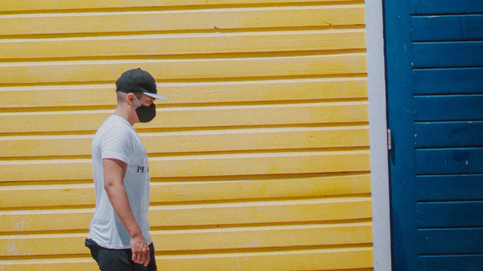 Person med munskydd går förbi en gul byggnad