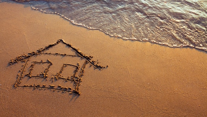 Hus ritat i sandstrand med vatten nära