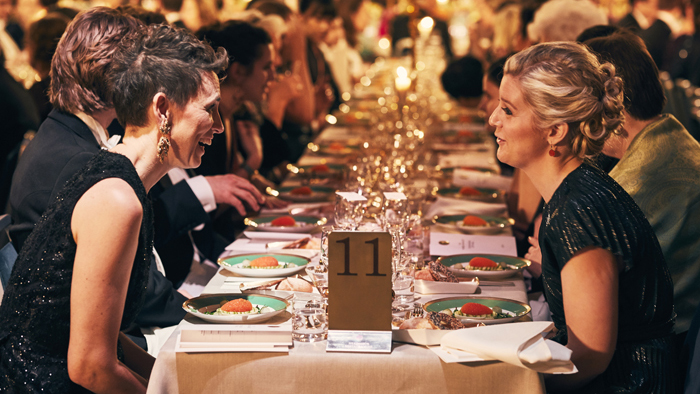 Ett dukat middagsbord på nobelbanketten med två kvinnor i fokus som samtalar över bordet. 