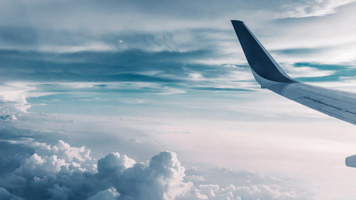 Vy från flygplan i luften ovanför molnen. Vingen från flygplanet syns till höger. 
