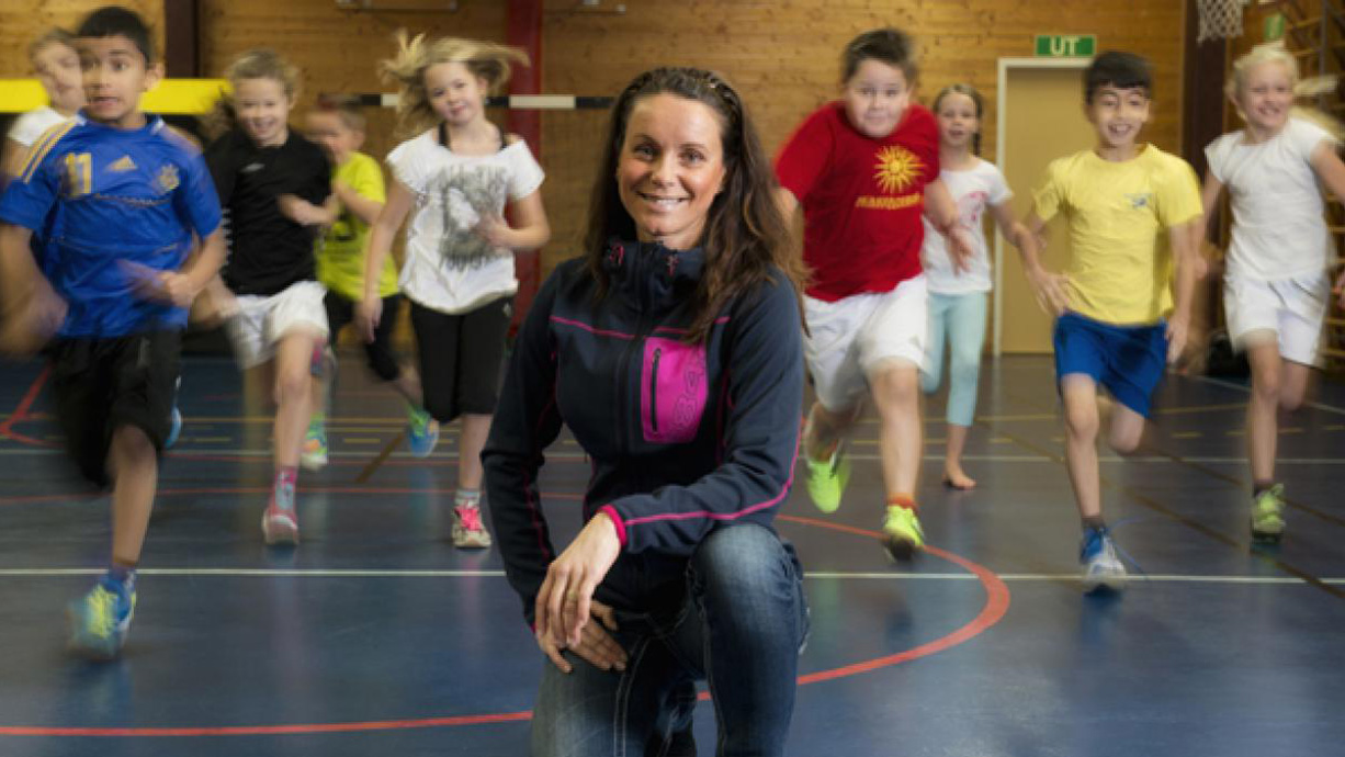 Lina Bunketorp Käll i gymnastiksal med skolelever som springer mot fotografen. 