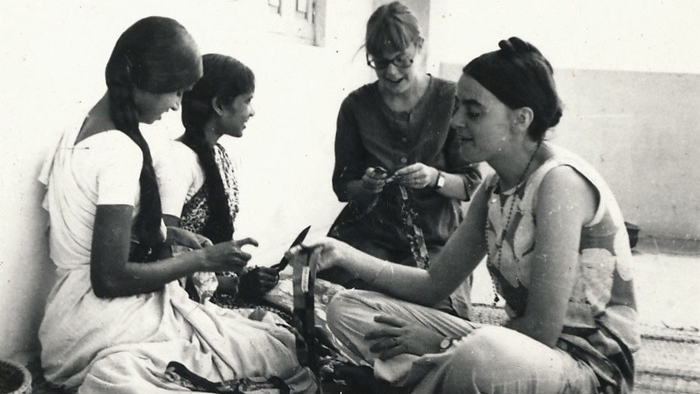 Fyra kvinnor sitter tillsammans på ett golv och handarbetar.