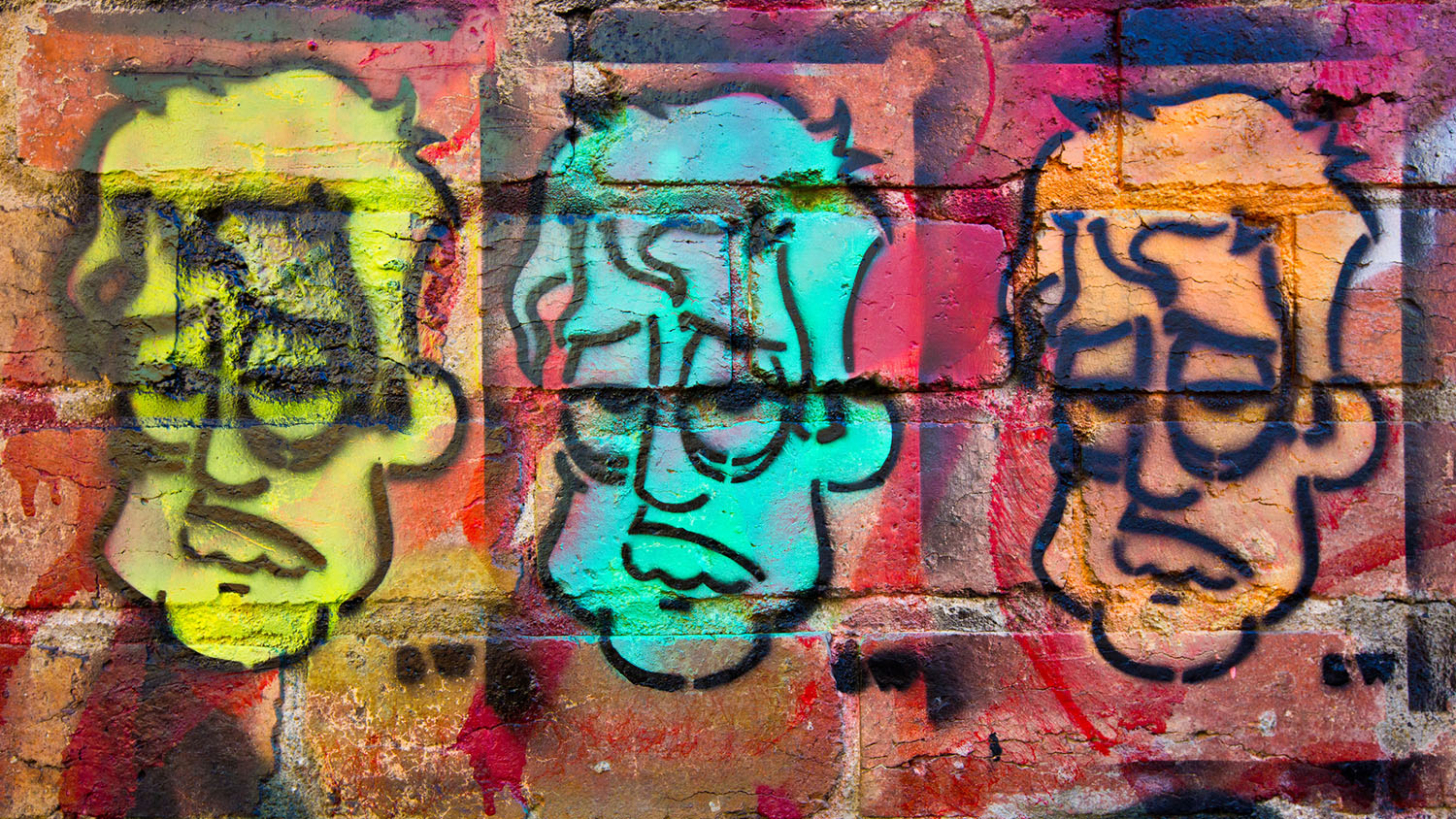 Graffiti med tre ansikten på en röd tegelvägg