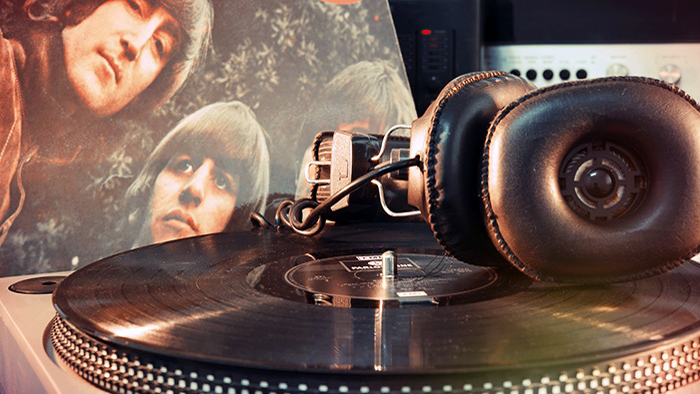 Ett par hörlurar ligger på en analog skivspelare. I bakgrunden syns omslaget till ett Beatlesalbum.