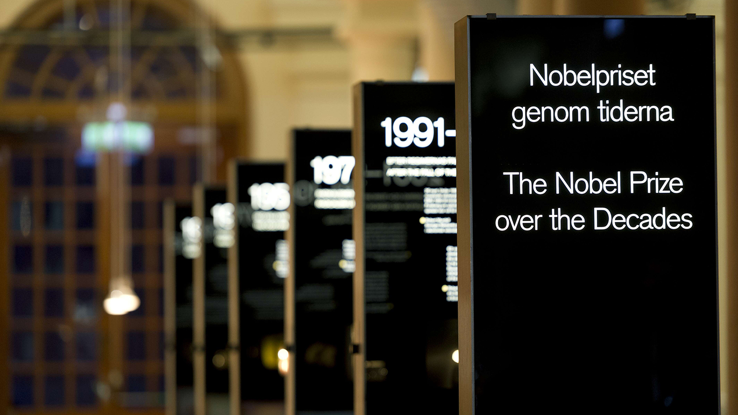Svarta utställningsskyltar där texten på den närmaste lyder "Nobelpriset genom tiderna" 