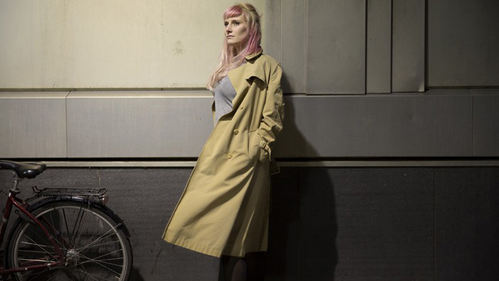 Isabelle Ståhl bär en kappa och står mot en vägg, till vänster syns bakhjulet på en cykel.