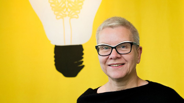 Eva Hemmung Wirtén står mot en gul bakgrund med en målad glödlampa.